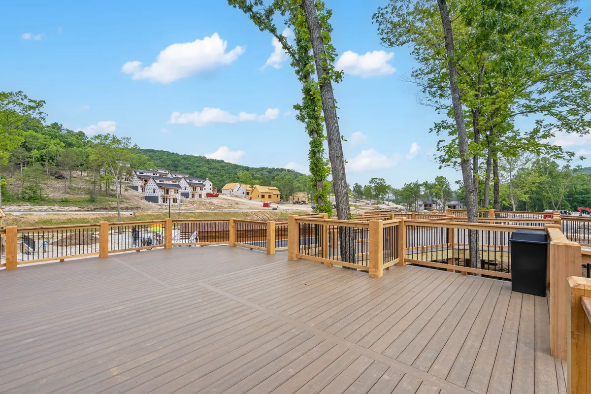 This exterior image features a wooden deck framed by tall trees, with ample space for outdoor dining, socializing, and unwinding. The view includes neighboring houses and the peaceful ambiance of the forested resort setting.