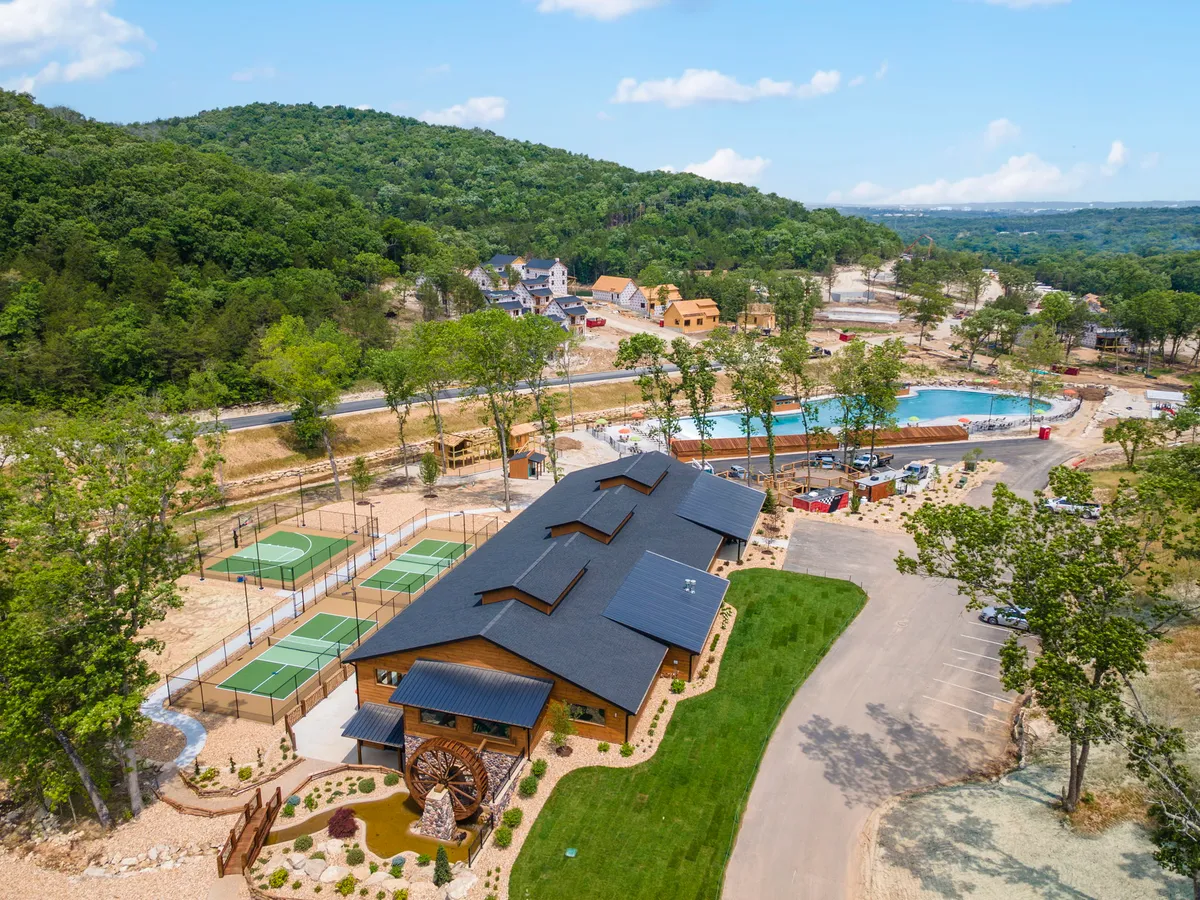 This exterior image captures the community center building, swimming pool, tennis courts, and nature trails set against a picturesque mountain backdrop. The scene radiates a lively, communal atmosphere, with facilities that encourage both relaxation and active family fun.