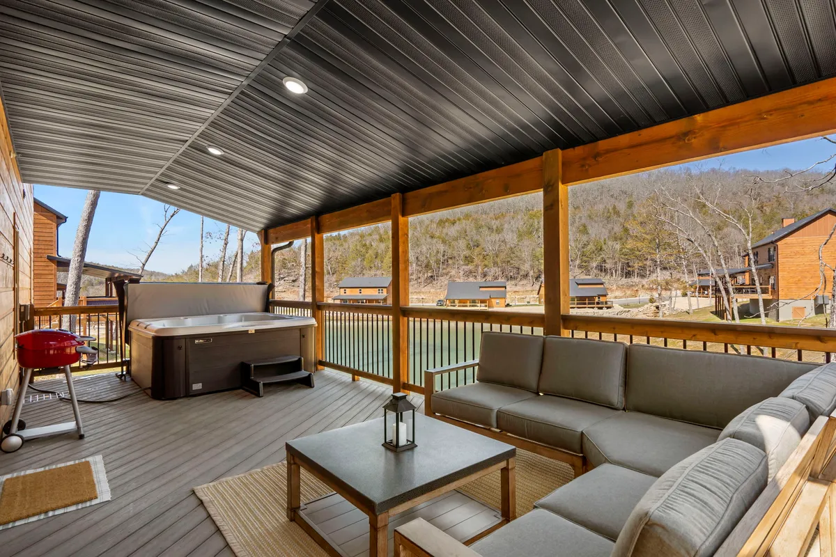 This exterior shot captures a spacious deck featuring a bubbling hot tub, an outdoor seating area, a grill, and sweeping views of the lush surrounding landscape. The soft, inviting lighting suggests a welcoming atmosphere perfect for relaxing after a day exploring the Ozarks.