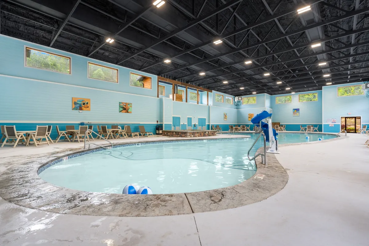 This image captures a bright, cheerful indoor pool area with lounge chairs, expansive windows letting in natural light, and vibrant artwork on the walls. The space exudes a lively, inviting atmosphere perfect for relaxation and recreation.