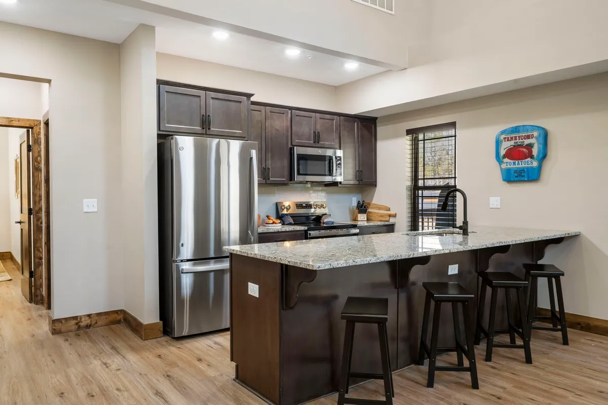 A modern kitchen showcasing a spacious island with granite countertops, stainless steel appliances, wooden cabinets, and decorative wall art. Bar stools invite casual conversation and group meal prep, making the kitchen a central hub for gatherings.