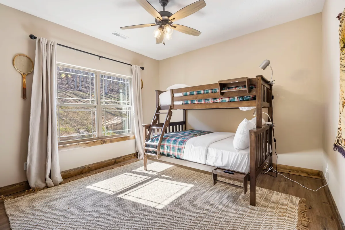 A playful bunk room with a bunk bed, a large window letting in lots of natural light, and a cozy rug. The room feels open and cheerful, perfect for kids or teens to enjoy their own space.