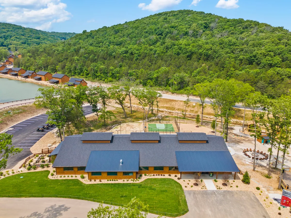The exterior view features the resort’s main building set against natural surroundings, including a basketball court, parking area, and glimpses of water. The scene is bustling with recreational energy, showing spaces for outdoor activities and gatherings.