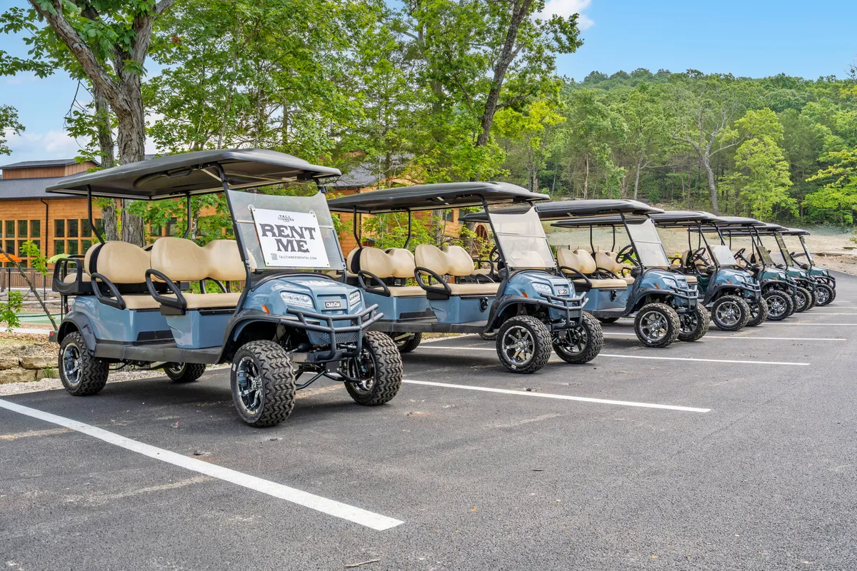 A lively exterior scene with golf carts waiting by a 'RENT ME' sign, surrounded by greenery and a building in the background. The scene suggests group outings, golfing, and the convenience of exploring the local area with friends or family.