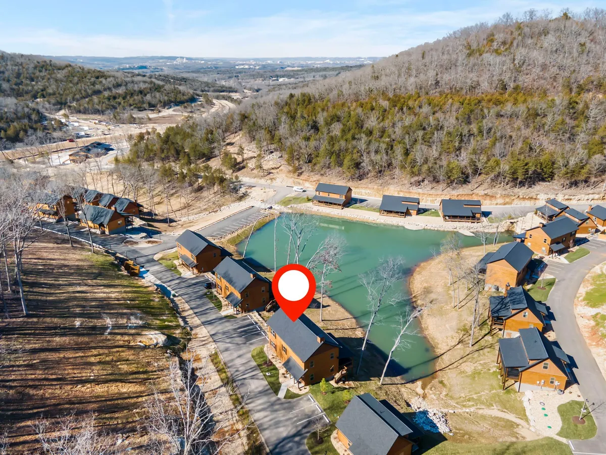 A tranquil exterior view of cabins nestled beside a serene pond, with trees and a quiet road winding through the property. The landscape encourages walks, relaxation, and enjoying the beauty of the outdoors.